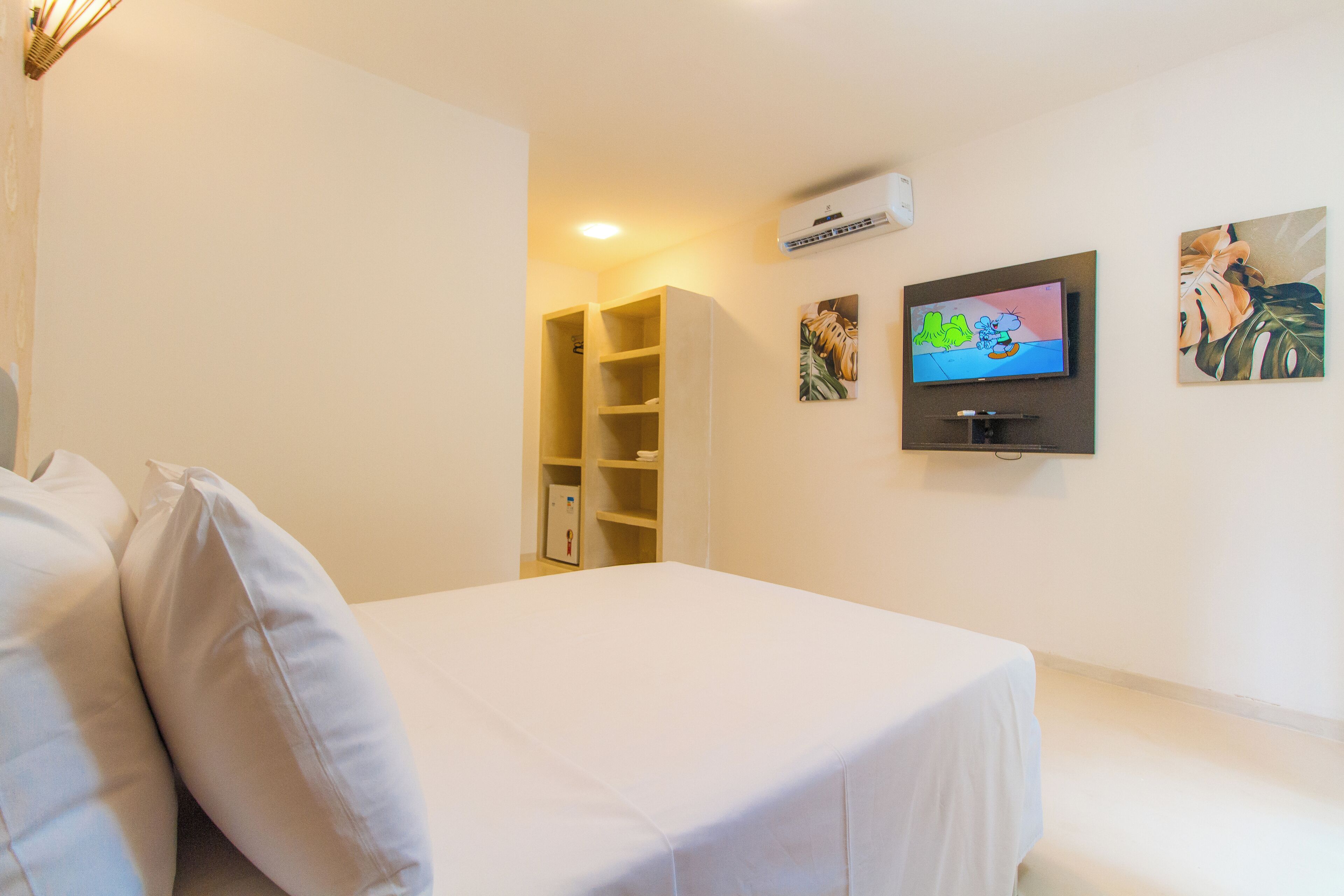 A hotel room with a bed, a TV mounted on the wall, and a shelf with books.