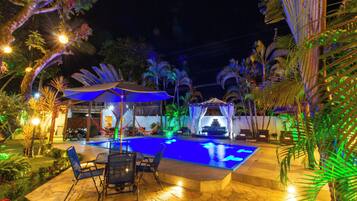 An outdoor swimming pool area with a seating arrangement and a covered area with a table and chairs.