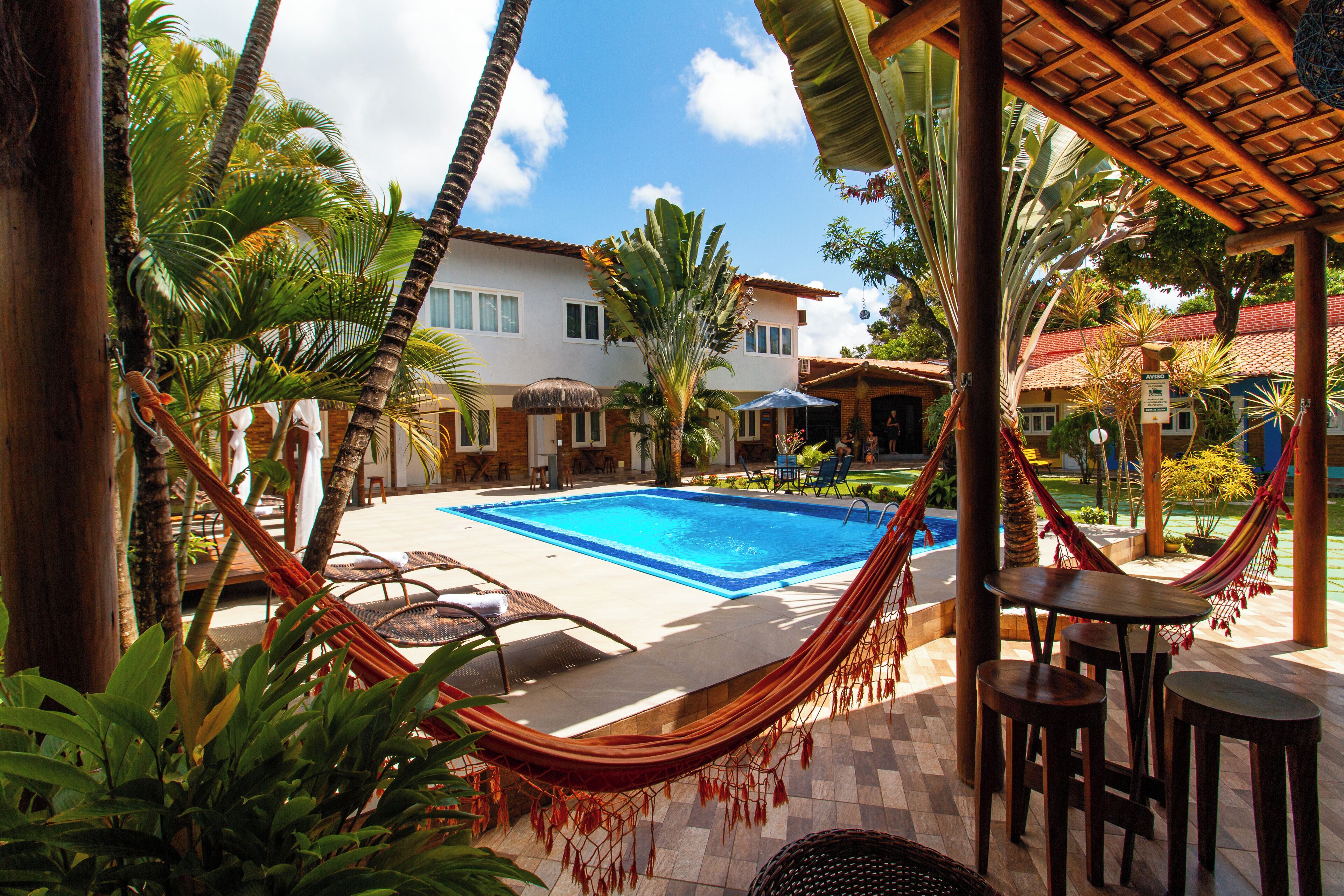 A pool area with a hammock, lounge chairs, and a thatched roof structure.
