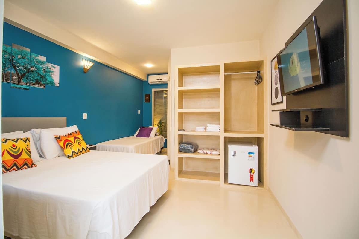 A hotel room with two beds, a TV, a wardrobe, and a small fridge.
