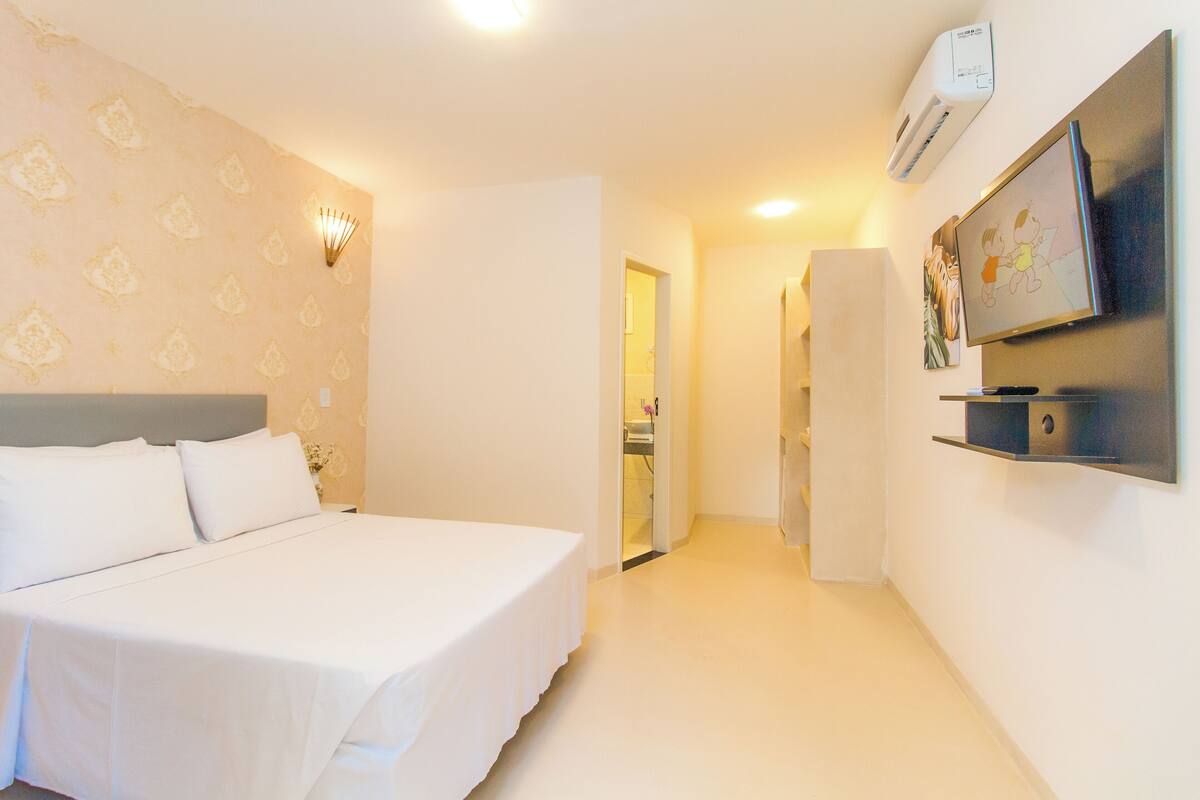A hotel room with a bed, a TV, and a wall-mounted shelf.