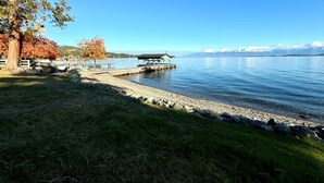 A lakeside view with a dock, a covered seating area, and a grassy area with trees. - Lakefront Estate w/ Private Beach on Flathead Lake (Lakeside)