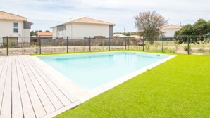 A rectangular swimming pool with a wooden deck and a grassy lawn. - Duplex apartment Mimizan plage (Mimizan)