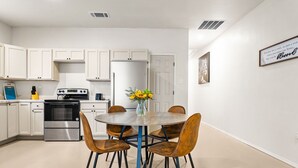 Een moderne keuken met witte kasten, een roestvrijstalen oven, een koelkast en een eettafel met vier stoelen.