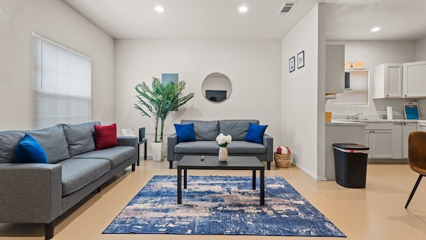 Een moderne woonkamer met een grijze bank, blauwe kussens, een bijzettafeltje en een blauw vloerkleed.
