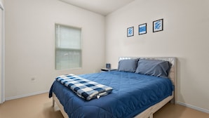 Een slaapkamer met een bed, een nachtkastje, een raam met jaloezieën en drie ingelijste foto's aan de muur.