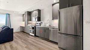 A modern kitchen with stainless steel appliances, grey cabinetry, and a wooden floor. - Six Flags/The Rim - Enchanting Modern Studio, King (San Antonio)