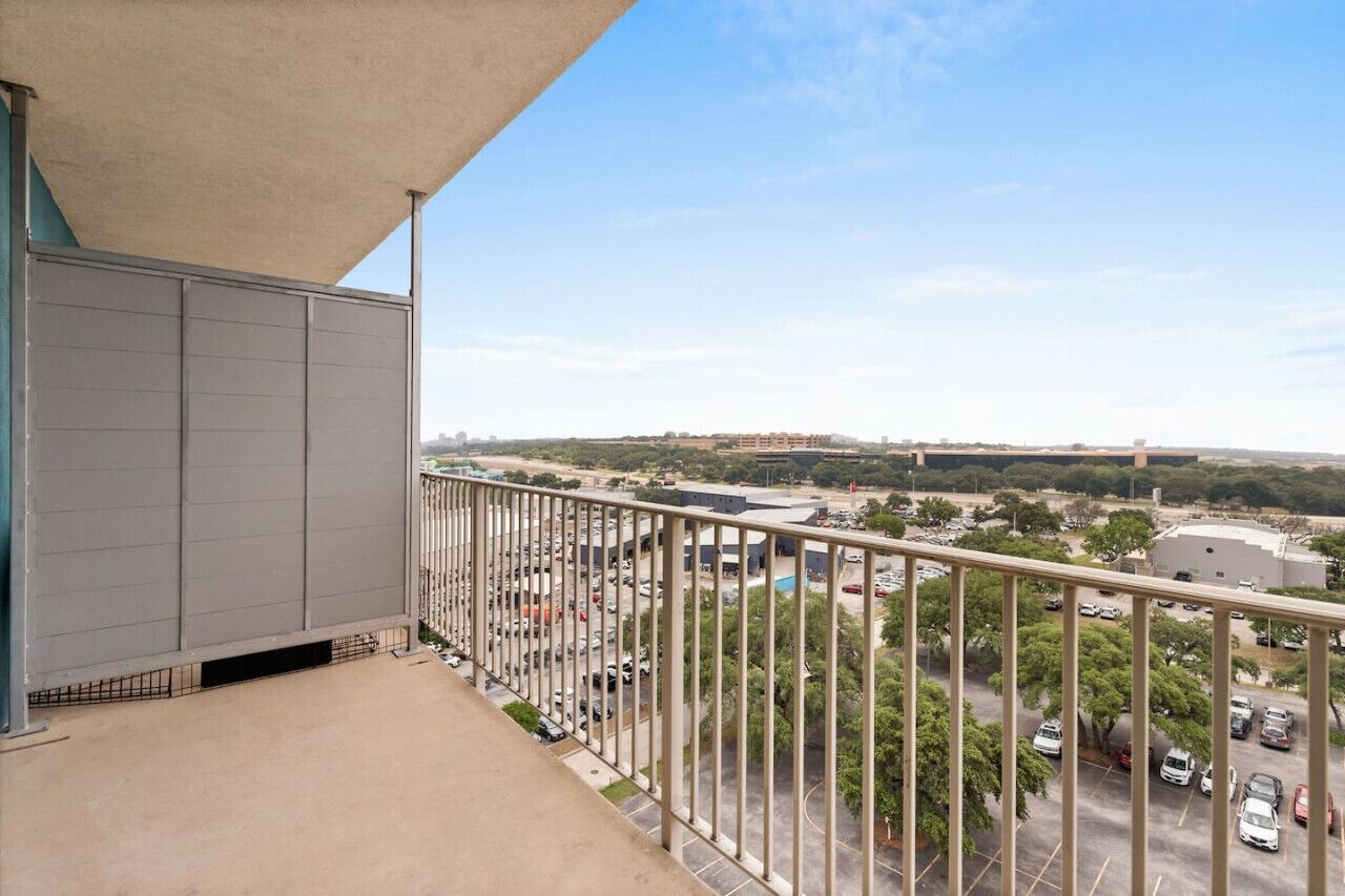A balcony with a view of a parking lot and buildings in the distance.