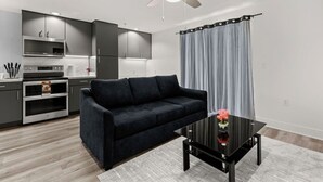 A modern kitchen with dark cabinets, a black sofa, and a glass coffee table. - Six Flags/The Rim - Chic Modern Studio, King Bed (San Antonio)
