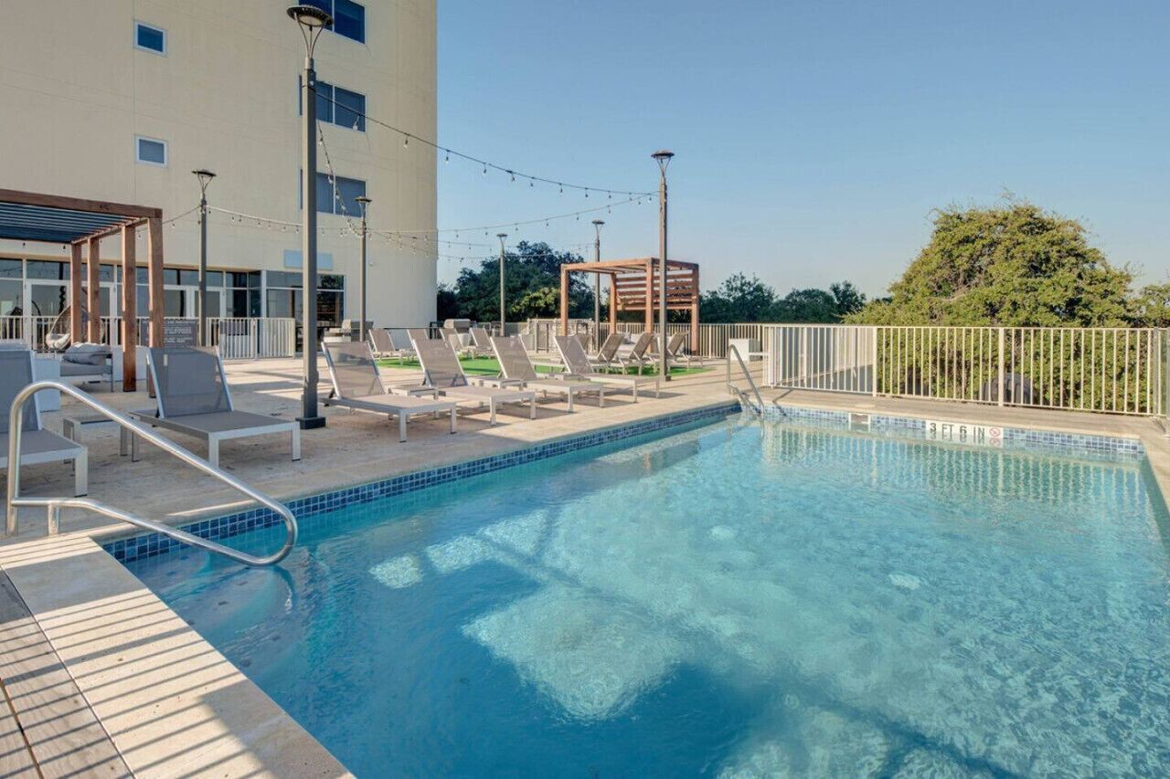 Une piscine dotée de chaises longues et d’une pergola, le tout entouré d’une clôture et d’arbres.