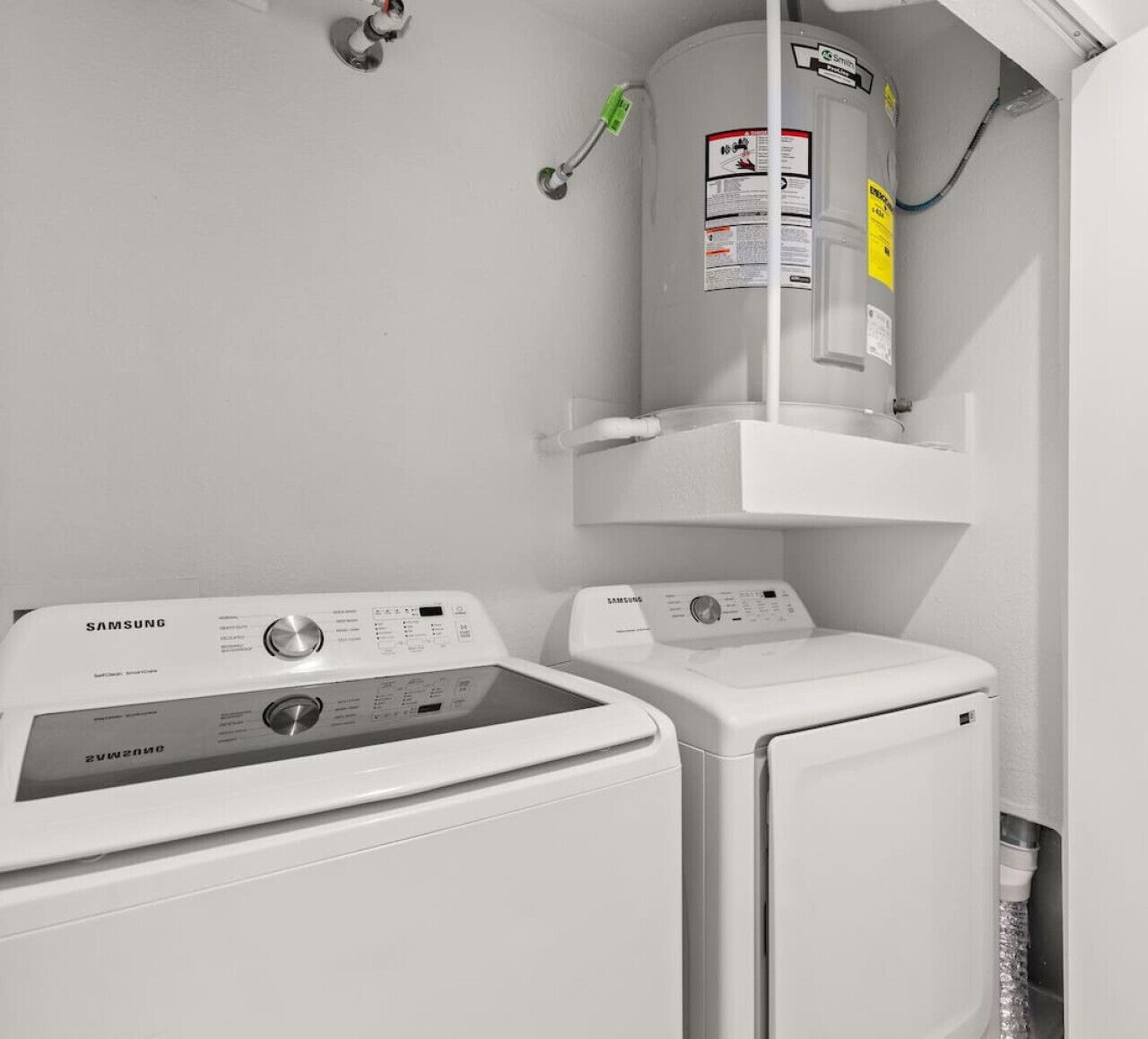A laundry area with two Samsung washing machines, a water heater, and a wall-mounted cabinet.