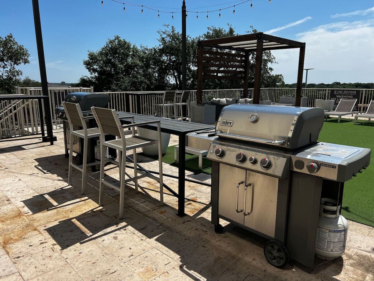 Une terrasse extérieure dotée d’un barbecue en acier inoxydable, d’une table avec des chaises et d’une structure en forme de pergola.