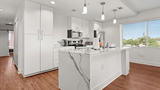 Une cuisine moderne avec des meubles blancs, un îlot en marbre et des luminaires suspendus.