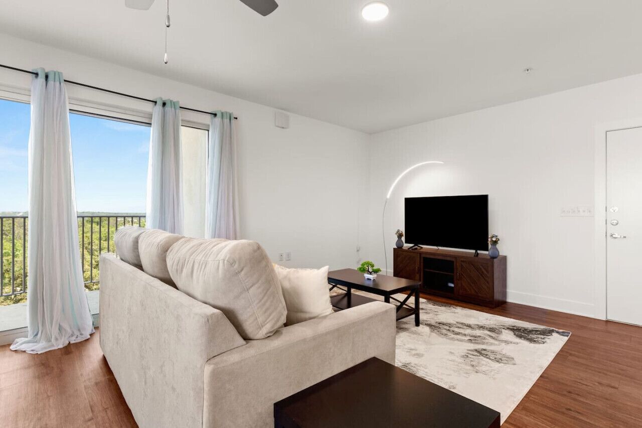 A modern living room with a sofa, a coffee table, and a flat-screen TV on a wooden stand.