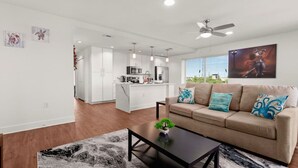 Un salon moderne avec un canapé beige, une table basse et, au fond, une vue sur la cuisine.