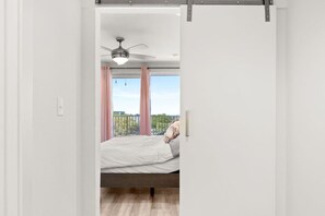 Un dormitorio con cama, ventilador de techo y vistas a un balcón con cortinas rosadas.