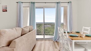 Ein modernes Wohnzimmer mit einem beigefarbenen Sofa, einem Holzesstisch mit weißen Stühlen und einem Balkon mit Blick.