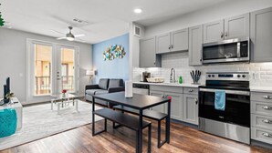 A modern kitchen with grey cabinets, a black microwave, and an oven. There is a dining table with benches in the center of the room. - Vibrant Oasis-Tower/Pool View, King Bed+ Free Park (San Antonio)