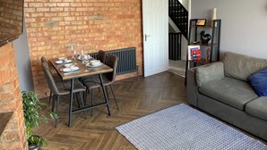 Un coin repas avec un mur en briques, une table dressée pour quatre personnes et un canapé dans l’espace salon.