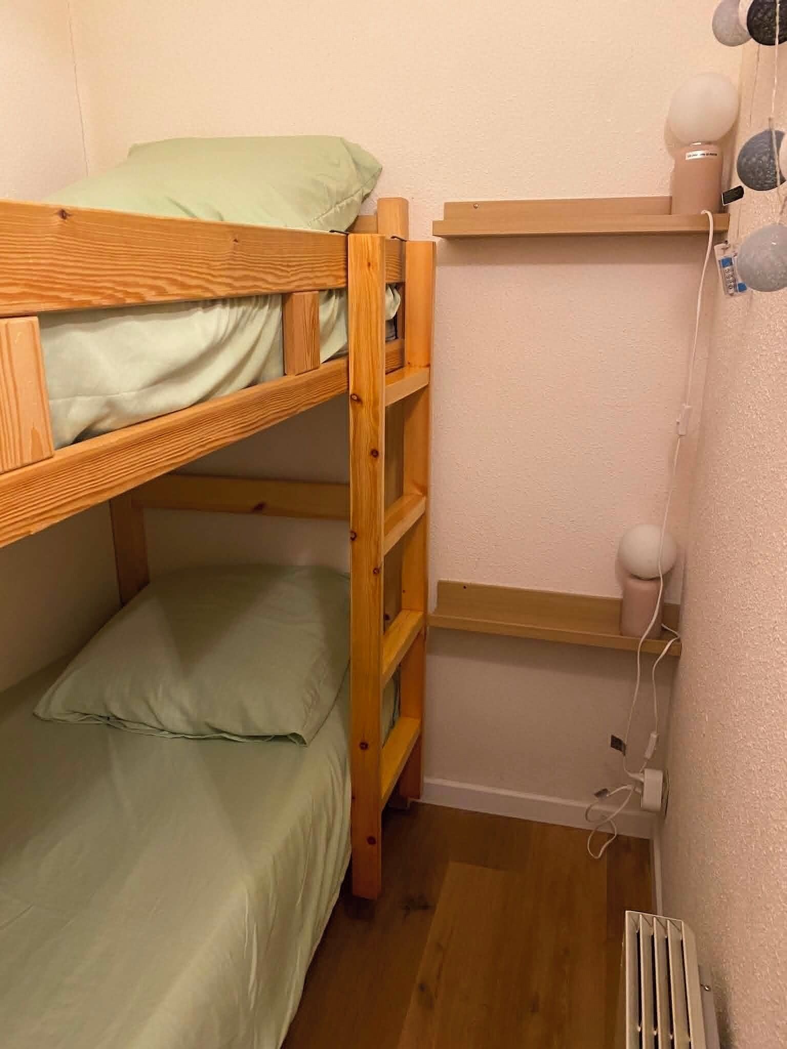 Una cama litera con escalera, un estante con lámpara y un radiador.