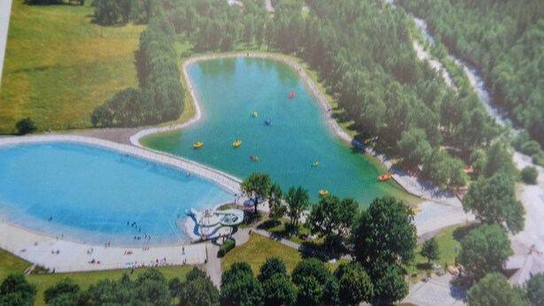 Luchtbeeld van een park met een groot meer, een speeltuin en een wandelpad.