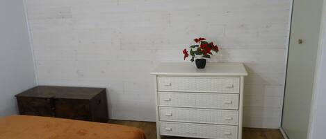 A room with a white dresser, a wooden chest, and a bed with an orange bedspread.