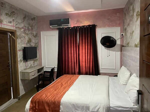 A bedroom with a bed, a desk, a chair, a TV, and an air conditioning unit. - Hotel Diego & Suites (Lekki)