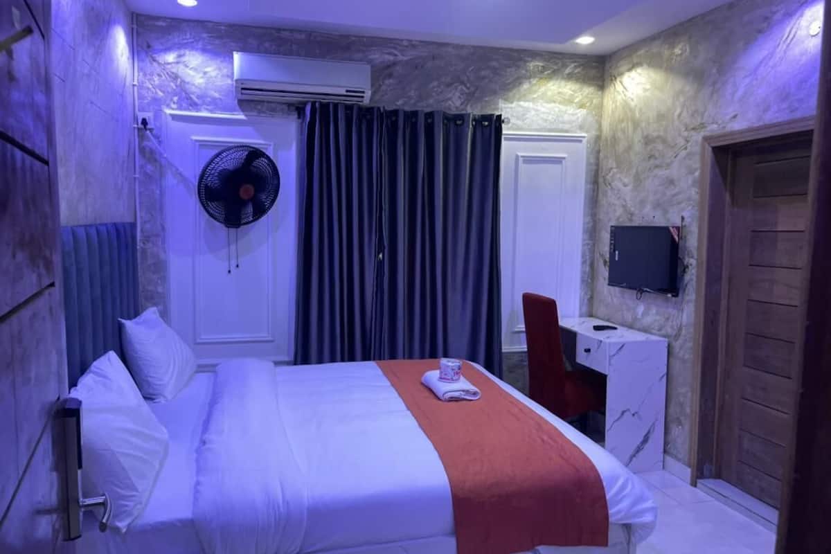 Una habitación de hotel con una cama, un escritorio, una silla, un ventilador y un televisor.