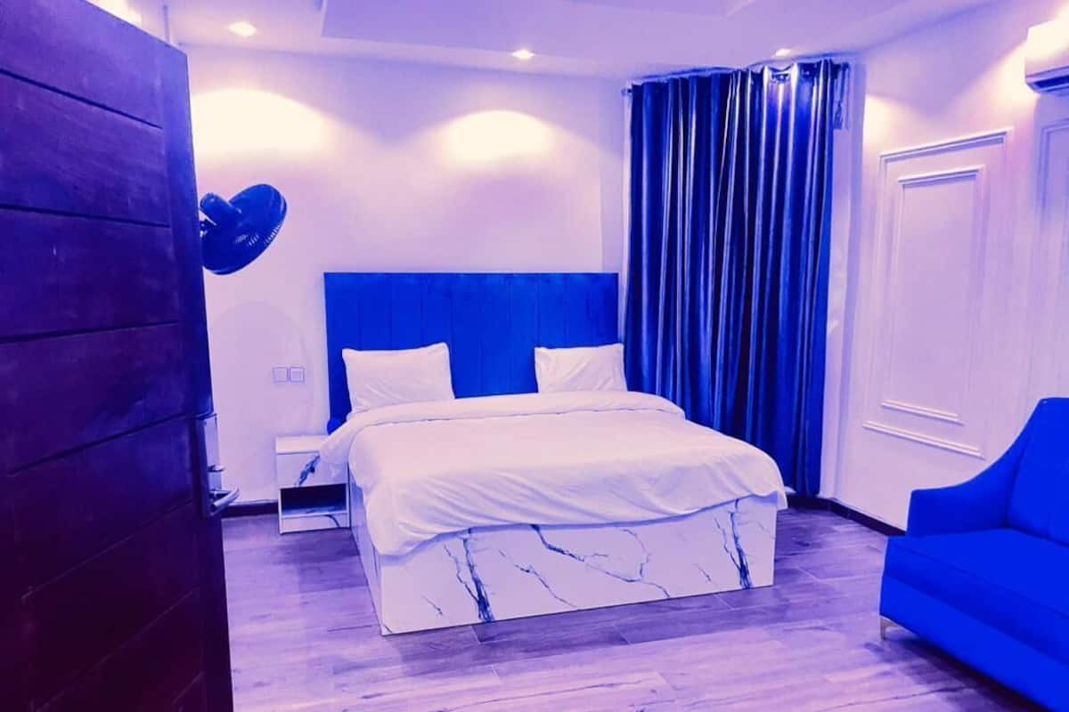 Un dormitorio con cama, mesita de noche, una silla azul y un armario de madera.