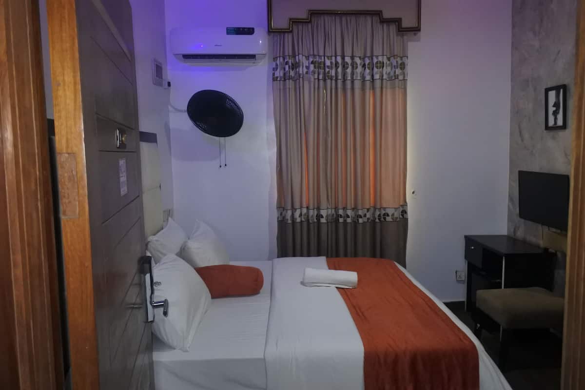 Habitación de hotel con cama, mesita de noche, aire acondicionado instalado en la pared, ventilador de techo y ventana con cortinas.