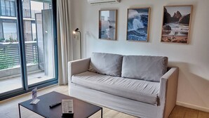 Ein modernes Wohnzimmer mit einer Couch, einem Couchtisch und einem Fernseher. An der Wand hängen drei Bilder und über der Couch befindet sich eine Klimaanlage.