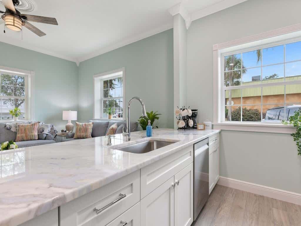 A kitchen with a marble countertop, white cabinets, a built-in dishwasher, and a window with a view of the outside.