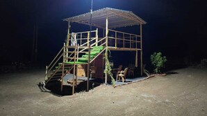 A small, elevated wooden structure with a staircase leading to a platform, surrounded by a dirt ground. - PAWS AT TIPESHWAR (Ghatanji)