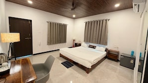 A hotel room with a wooden ceiling, a bed with white bedding, a desk with a lamp, and a small refrigerator. - PAWS AT TIPESHWAR (Ghatanji)