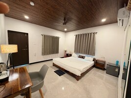 Habitación de hotel con techo de madera, cama con ropa blanca, escritorio con lámpara y un refrigerador pequeño.