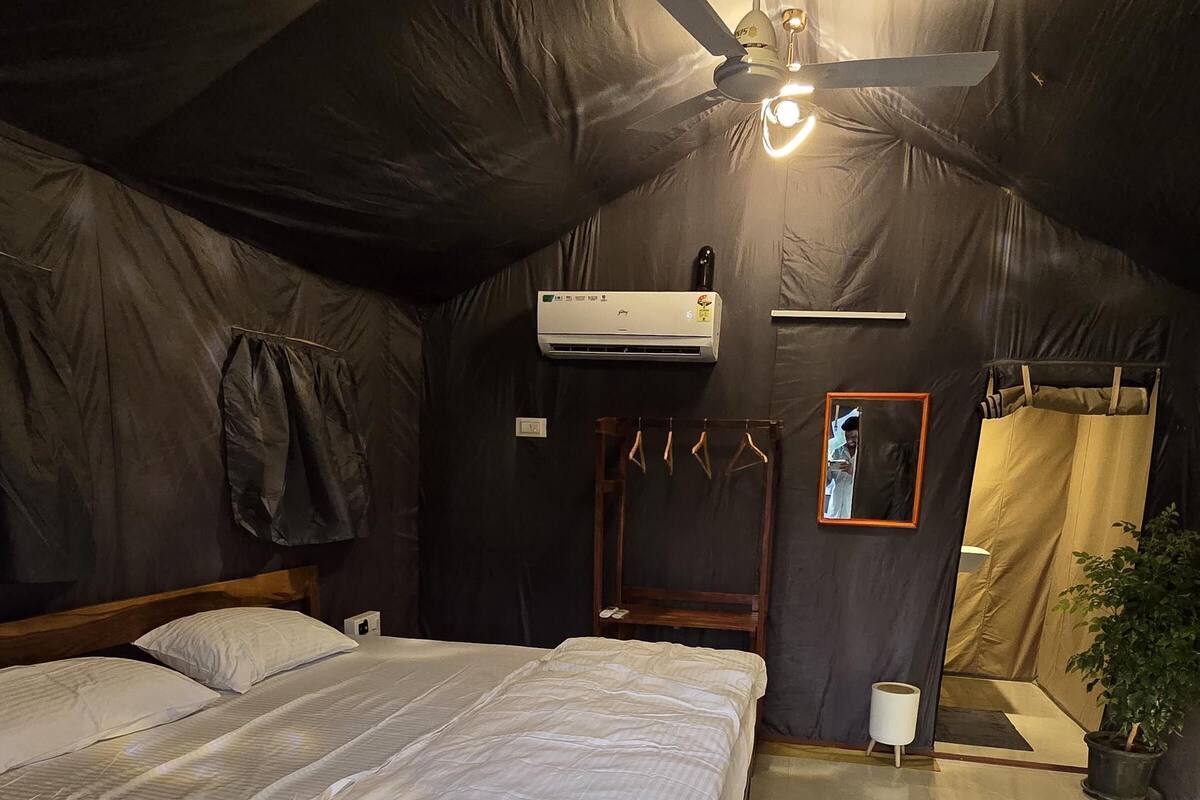 Ein Zelttyp-Zimmer mit einem Bett, einem Deckenventilator, einer Klimaanlage und einem kleinen Tisch.
