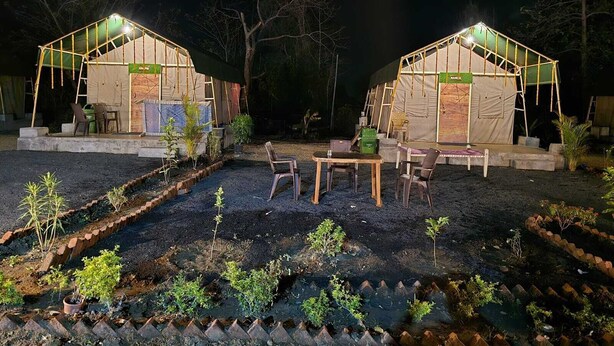 Two well-lit tents with tables and chairs, surrounded by a garden with young plants. - PAWS AT TIPESHWAR (Ghatanji)