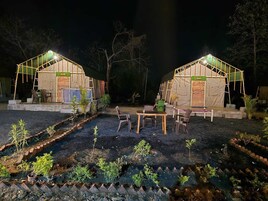 Dos tiendas bien iluminadas con mesas y sillas, rodeadas por un jardín con plantas jóvenes.
