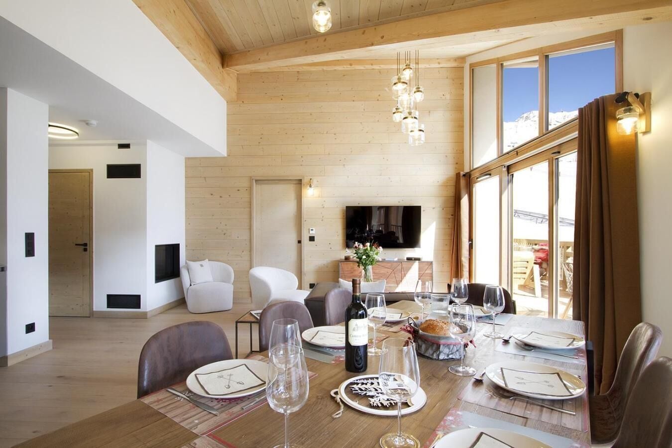 Ein moderner Essbereich mit einem Holztisch, gedeckt für eine Mahlzeit, einem Fernseher im Hintergrund und Blick ins Freie.