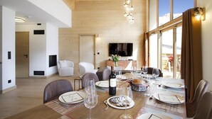 Un comedor moderno con una mesa de madera dispuesta para una comida, un televisor al fondo y vistas al exterior.