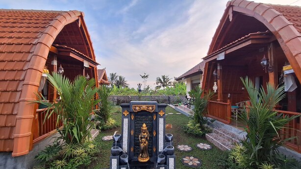 A traditional building with a central statue, surrounded by lush greenery and a tiled roof. - Green Pacing Lodge (Tembuku)
