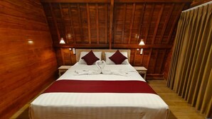 A wooden-paneled room with a large bed, two nightstands, and a red bedspread. - Green Pacing Lodge (Tembuku)