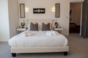 Een net opgemaakt bed met witte lakens en twee kussens, een nachtkastje met een wereldbol, en een wanddecoratie met de fasen van de maan.