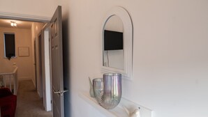 A hallway with a white door, a mirror, and a shelf with decorative items. - House - Sleeps 7 - Parking - Garden - Near Stn (Manchester)
