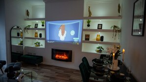A modern living room with a fireplace, a television mounted on the wall, and shelves with decorative items. - House - Sleeps 7 - Parking - Garden - Near Stn (Manchester)