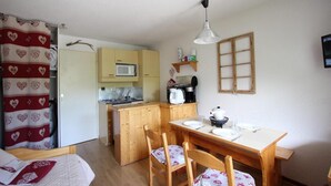 A compact kitchen with a microwave, stove, and coffee maker. There is a wooden dining table with chairs and a small island.