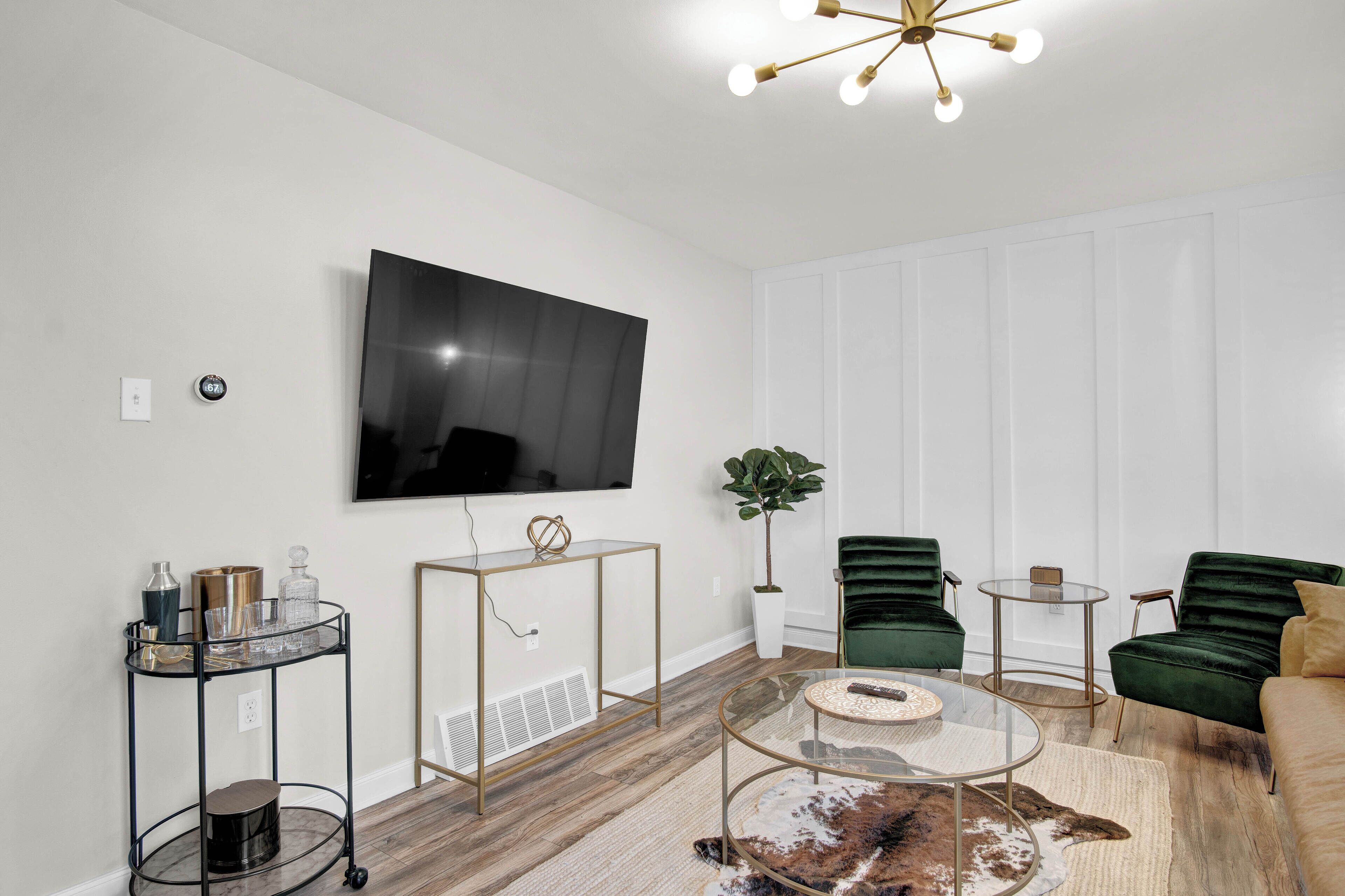 Una sala de estar moderna con un televisor de pantalla plana, sillones de terciopelo verde, una mesa de centro de vidrio y una alfombra decorativa.