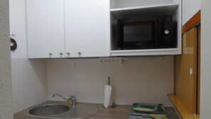 Uma cozinha compacta com pia, micro-ondas e escorredor de louça.