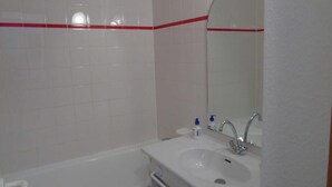 Casa de banho com azulejos brancos, uma banheira, um lavatório com espelho e uma faixa vermelha na parede.