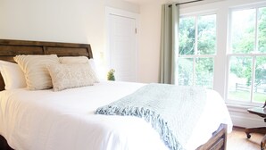Een groot bed met een houten hoofdbord, witte beddengoed en een lichtblauwe plaid.